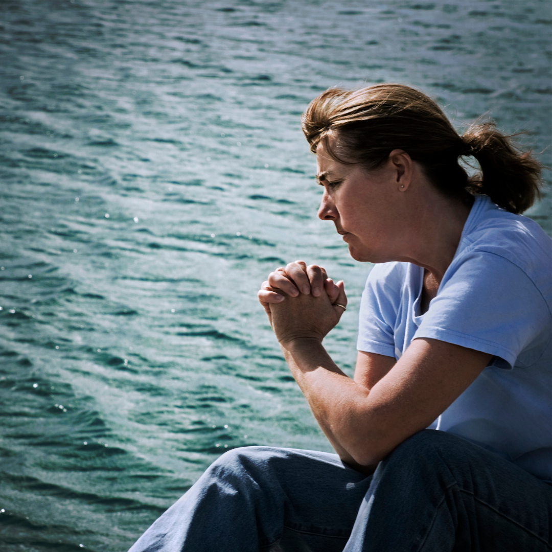 woman praying next to a lake