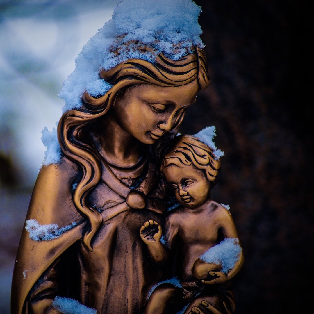 bronze statue of Mary holding baby Jesus, both covered in snow