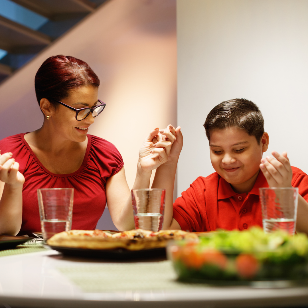 Family praying before meal at dinner table with food and drinks