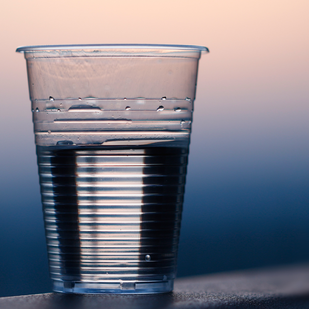 Clear cup half-filled with water, with blurred sunset background