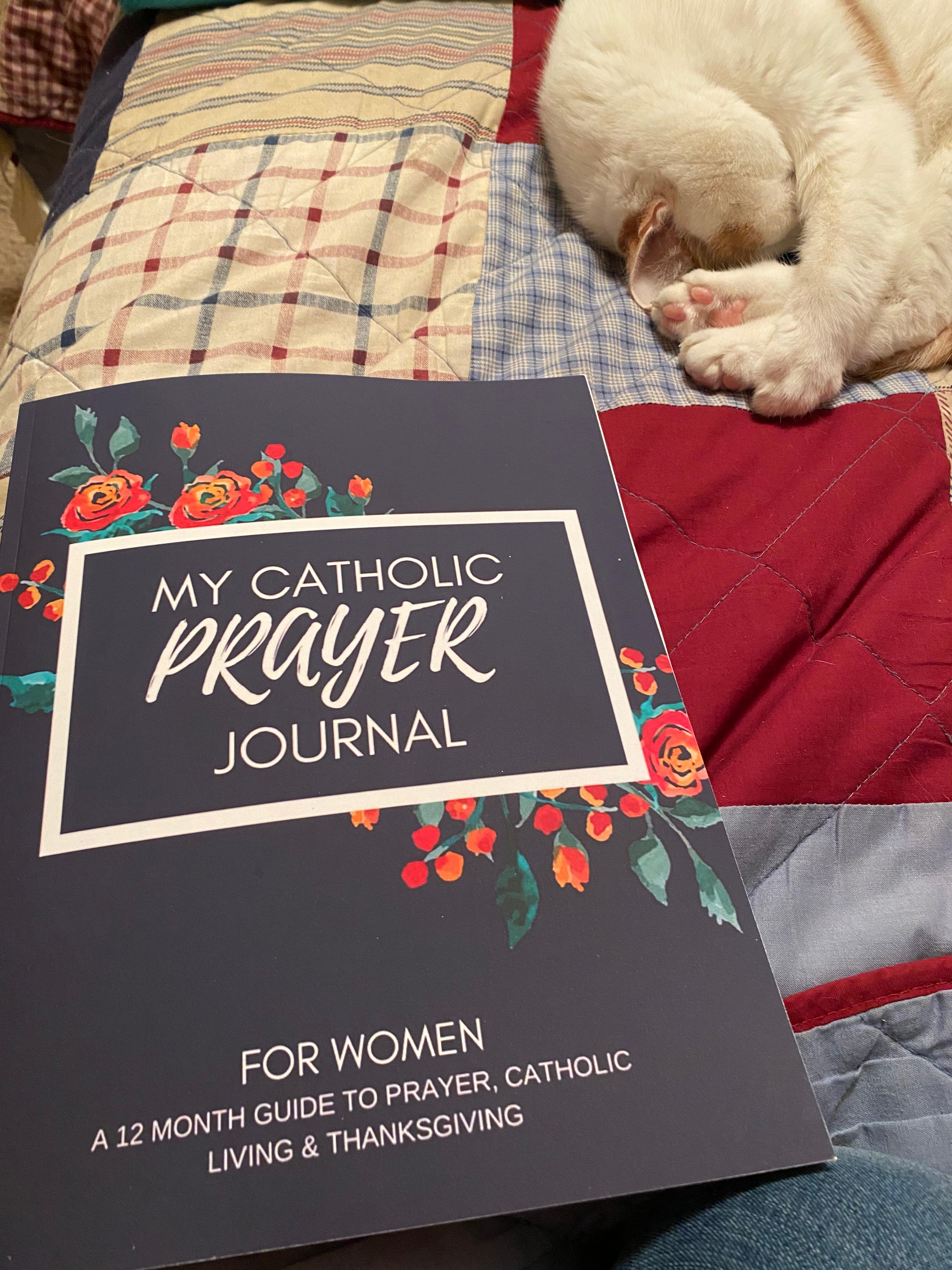 Catholic Prayer Journal for women on red, white, and blue quilt, with white cat sleeping