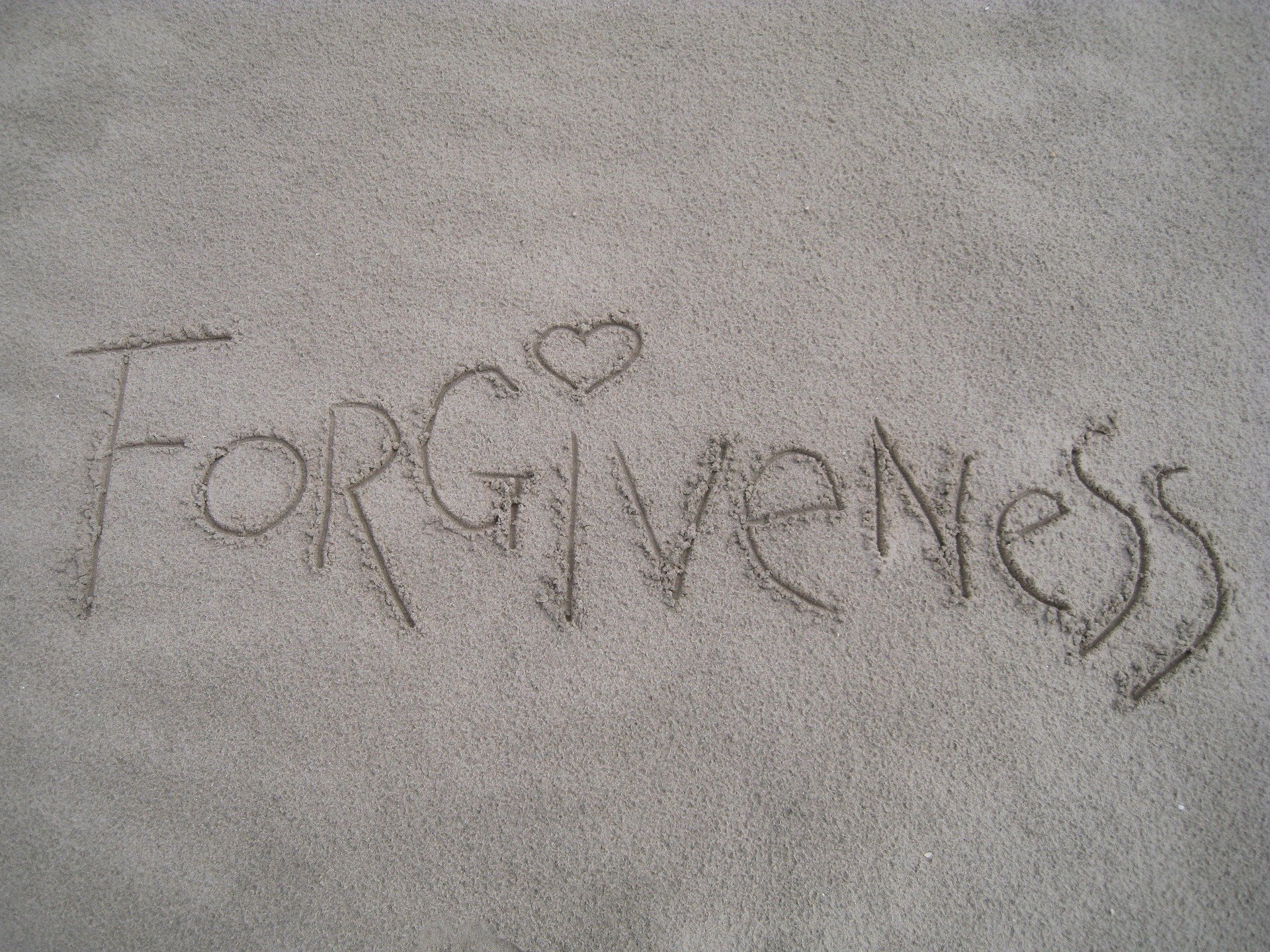 sandy beach with the word "forgiveness" written on it, with a heart above the letter I