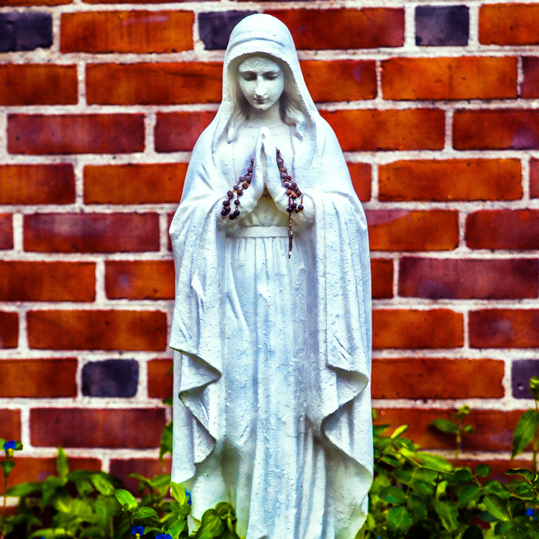 statue of Mary with Rosary over her hands, brick wall behind