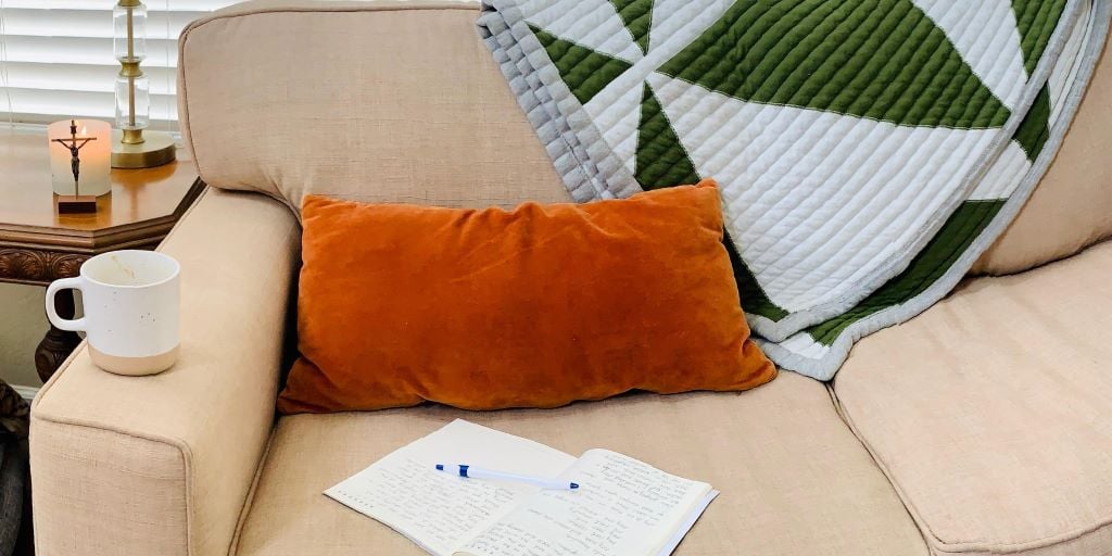 coffee mug, journal, pillow, and blanket on couch