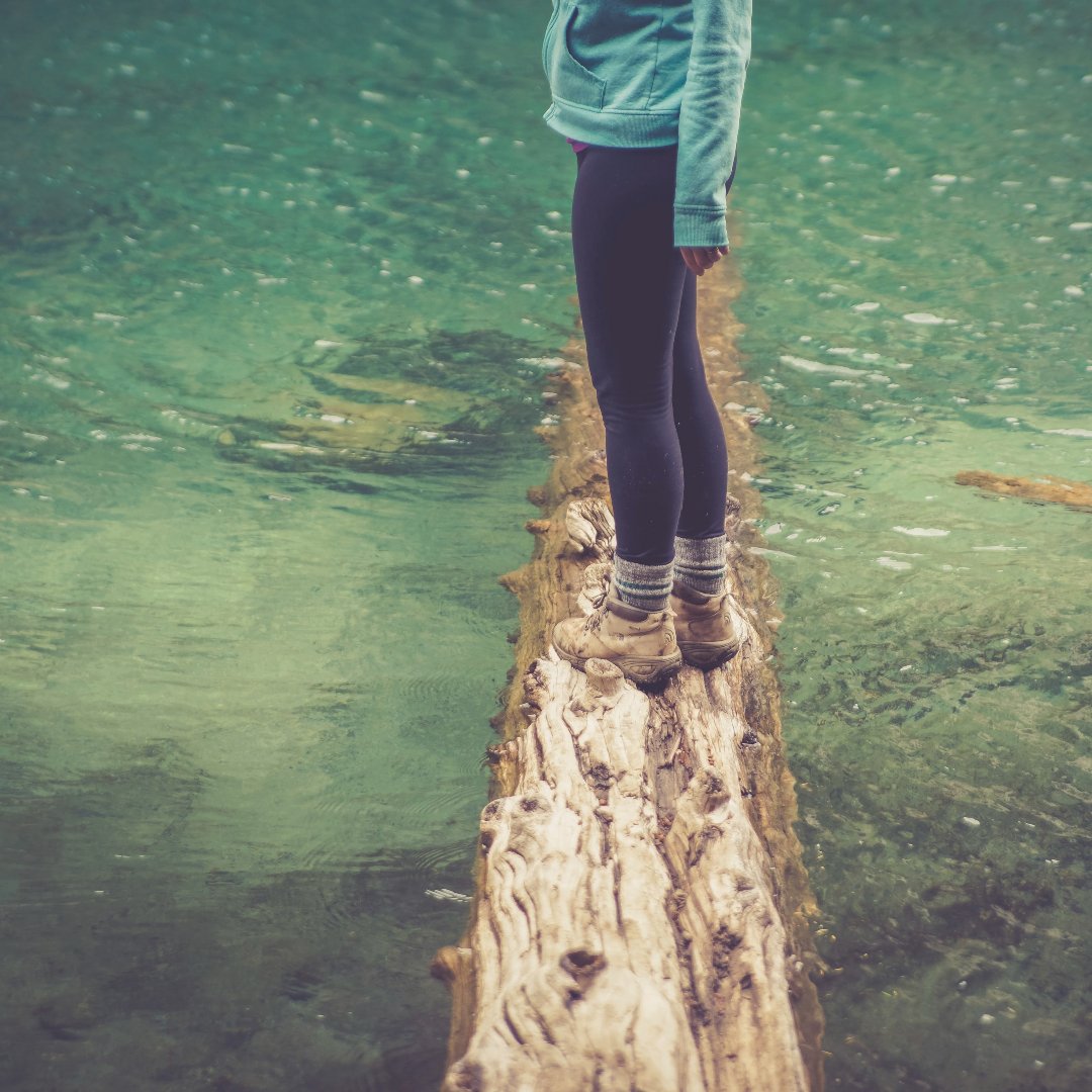 Woman wearing hiking boots balancing on a fallen log over a pond