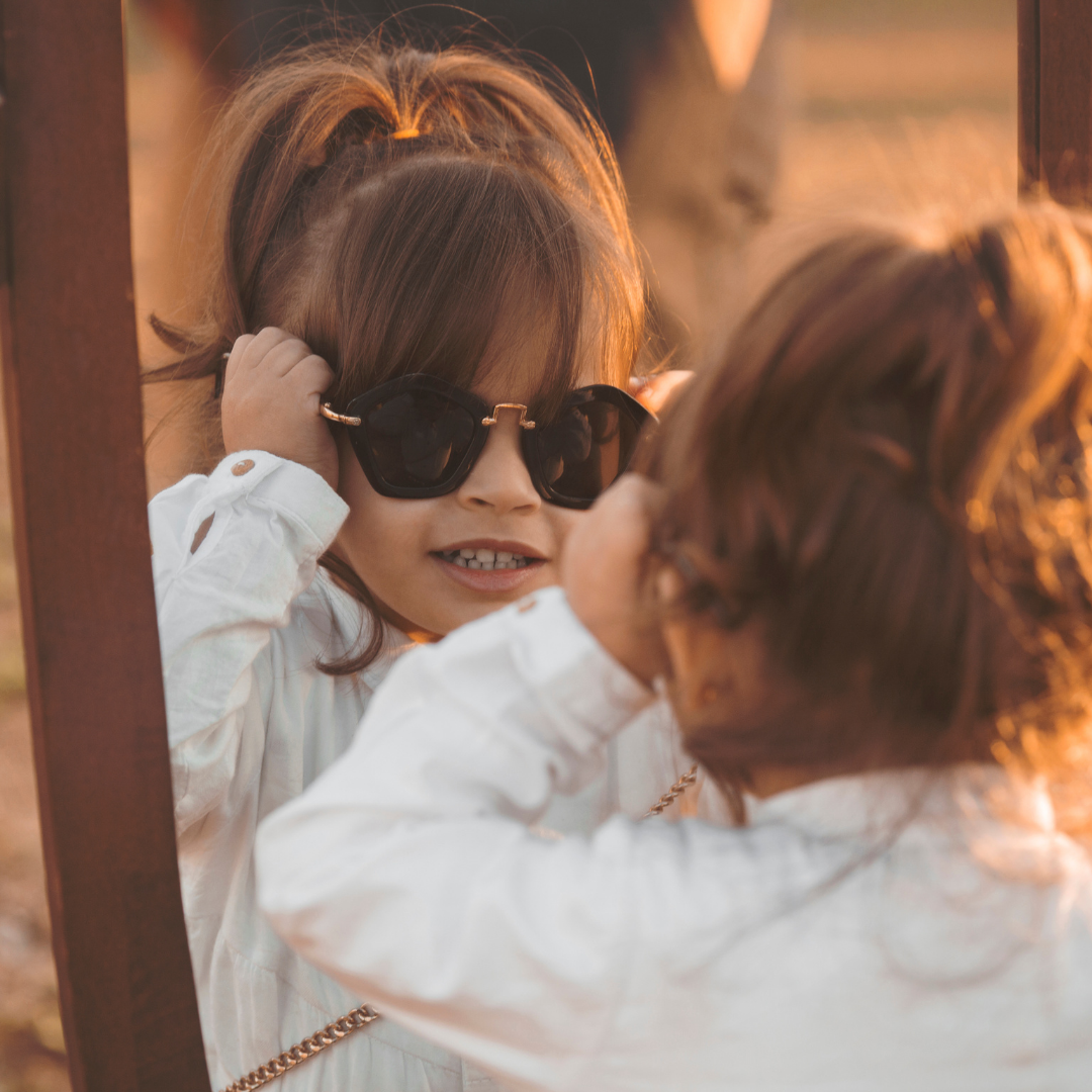 little girl trying on sunglasses in front of a mirror