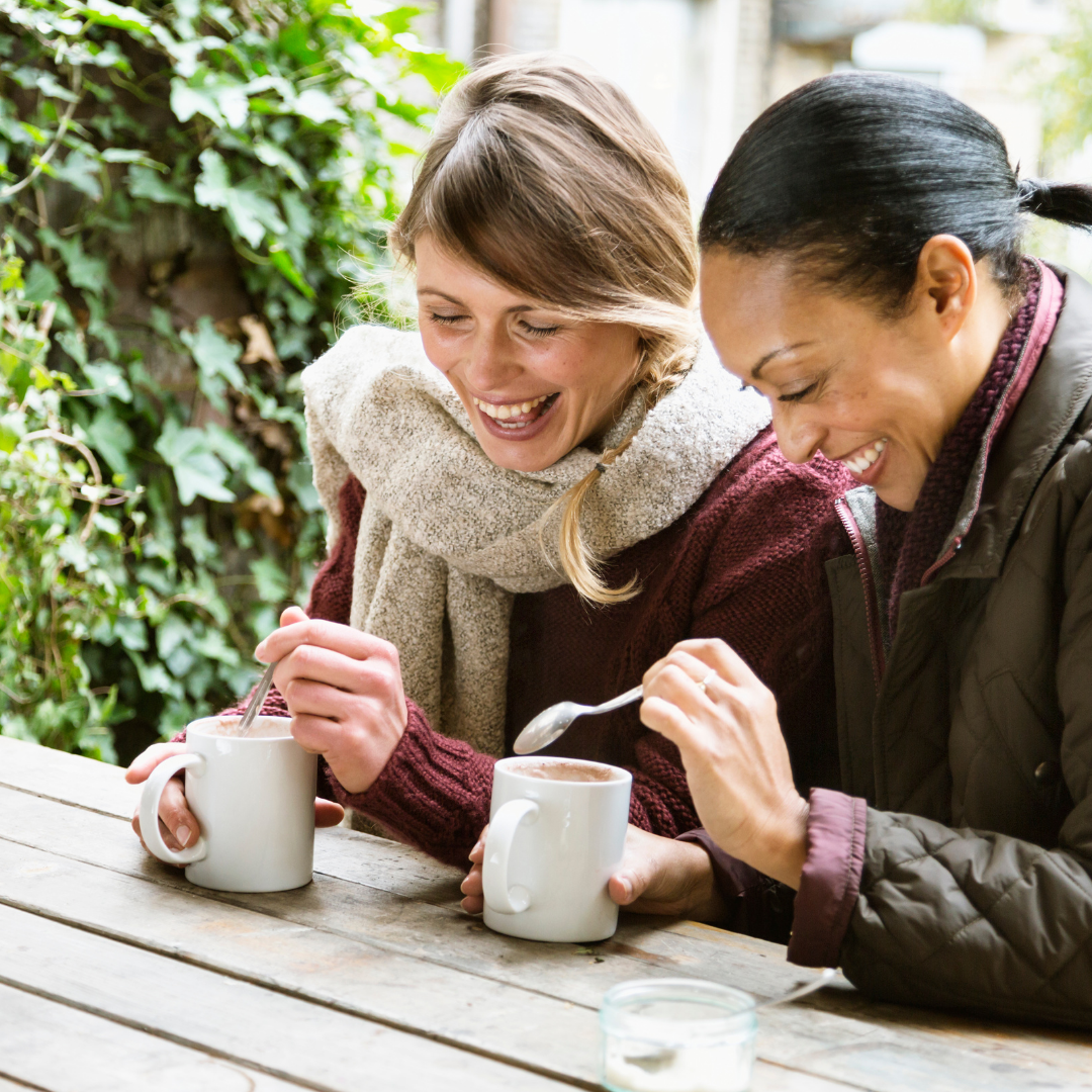 2 women smiling, stirring cups of coffee