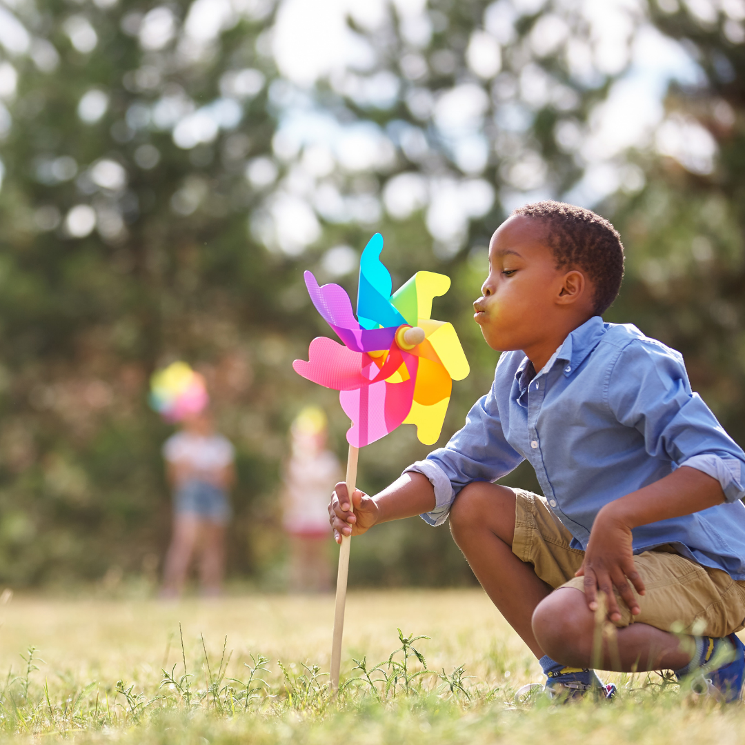 child in a field blowing on colorful pinwheel