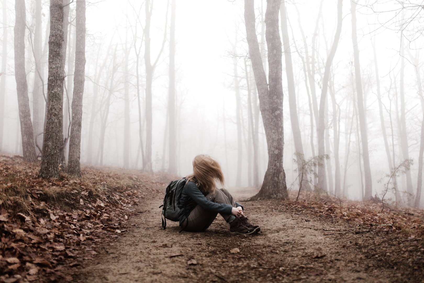 teenage girl with backpack sitting on forest floor