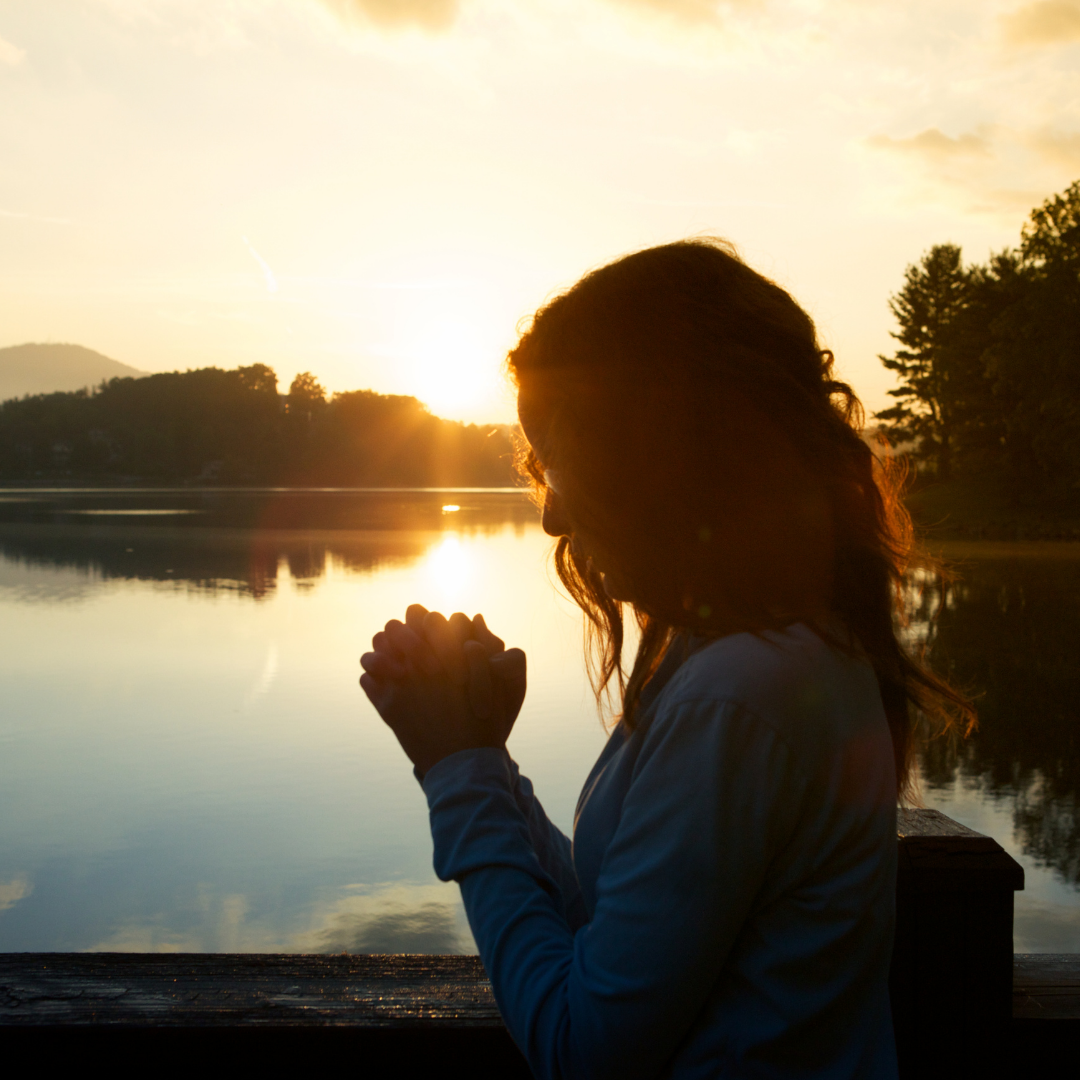 woman praying in front of a lake at sunrise