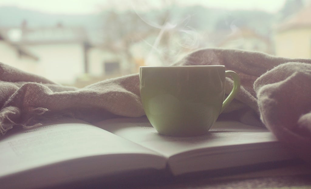 steaming coffee cup on top of open book and blanket