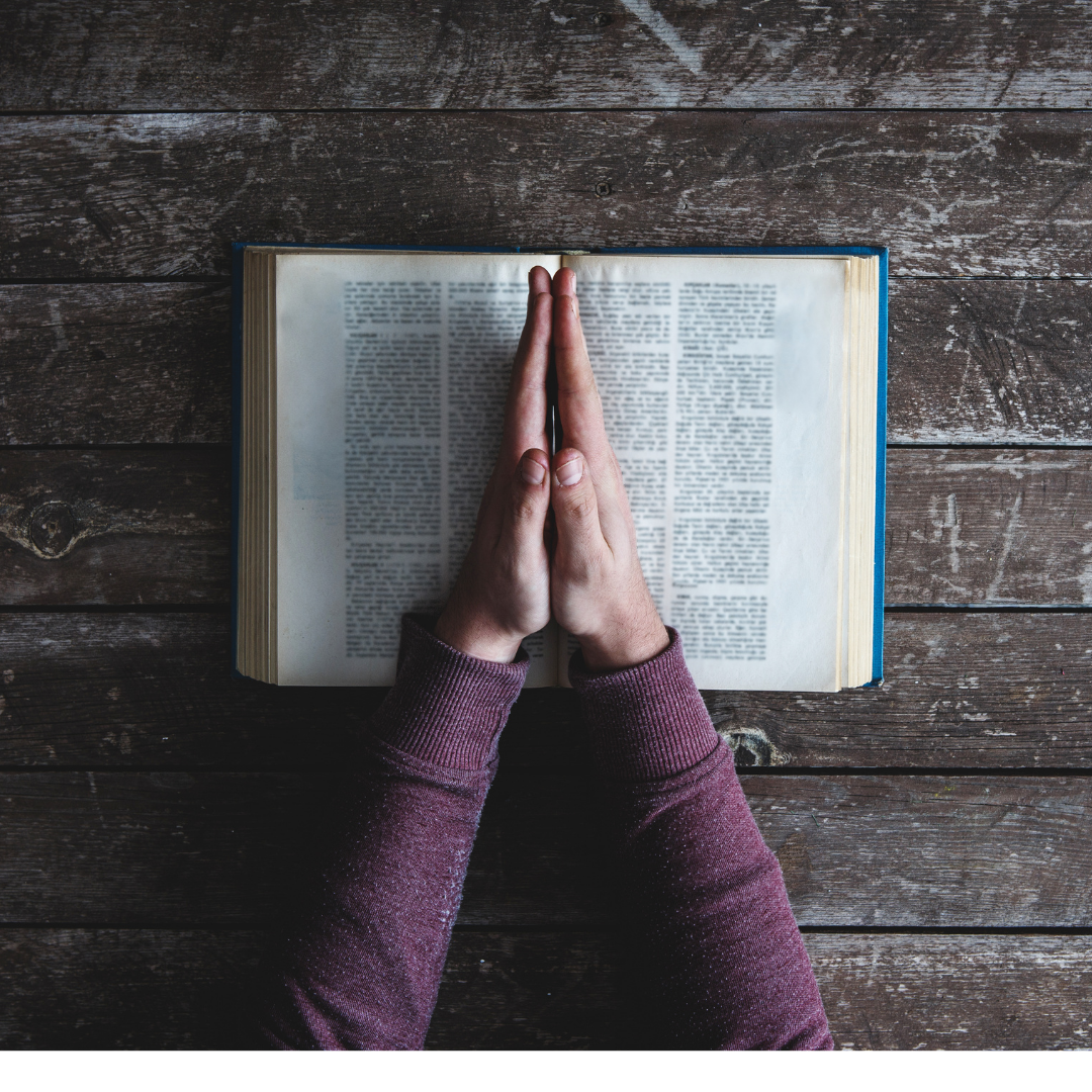 praying hands on top of Bible