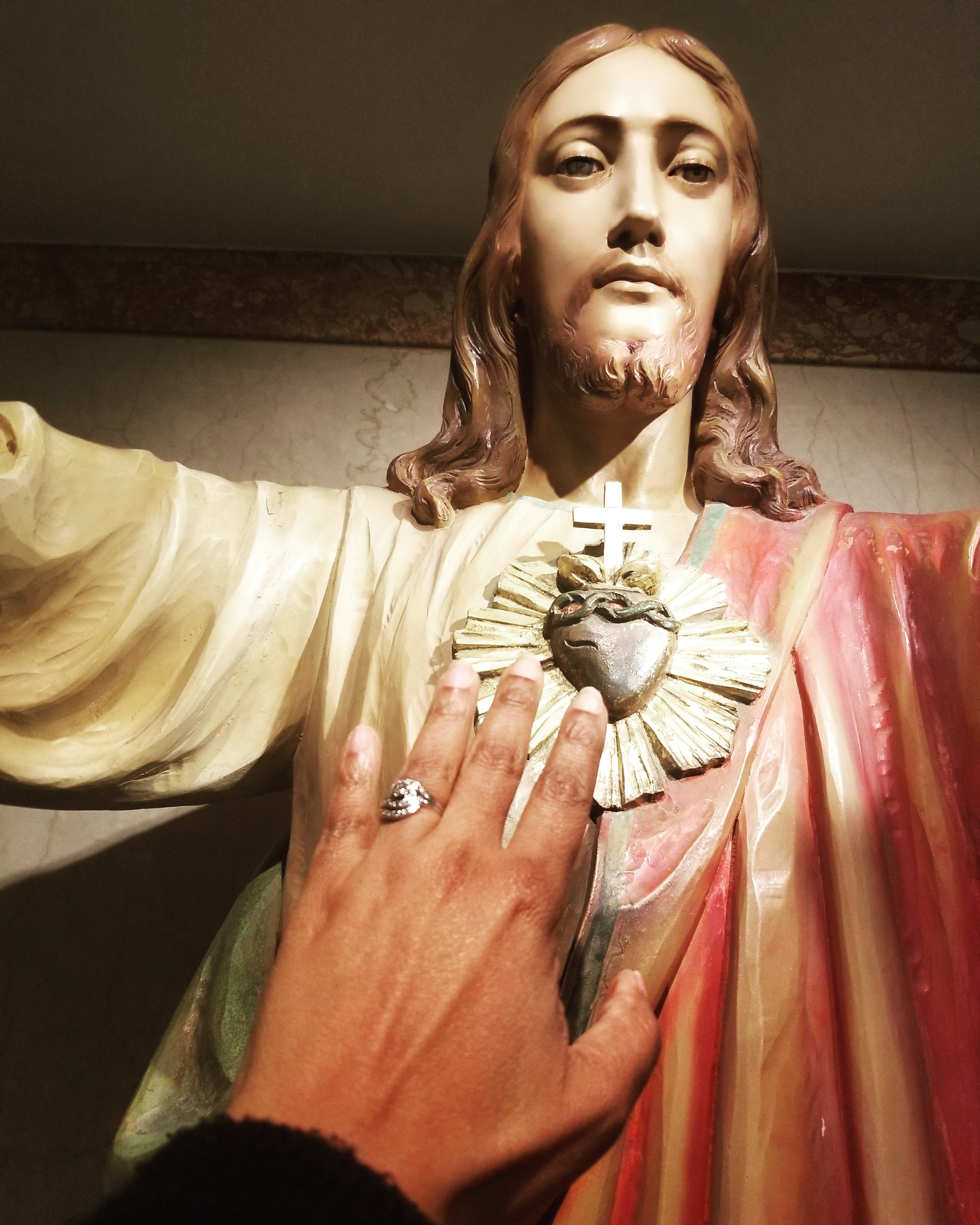 woman's hand touching Sacred Heart of Jesus statue