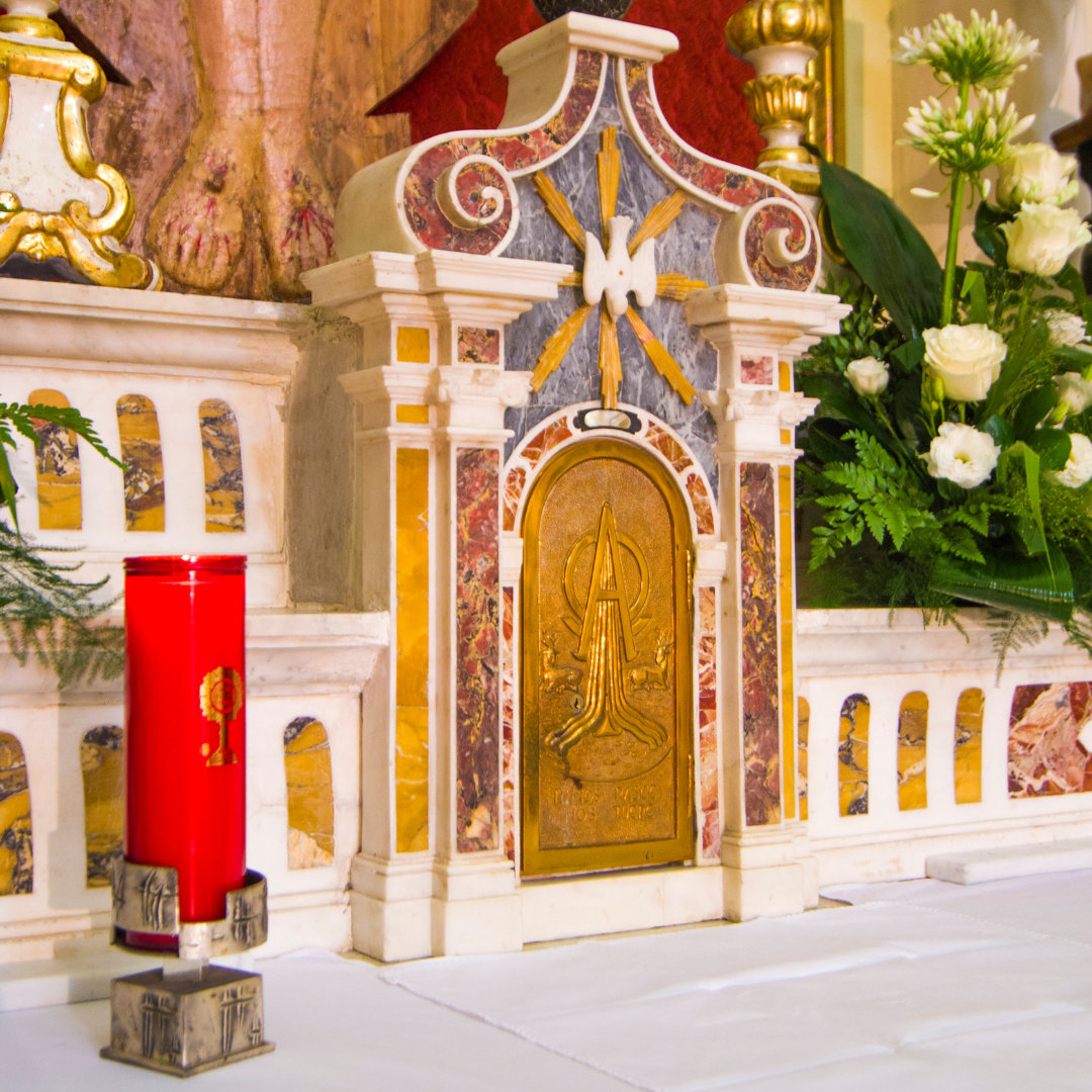 Gold tabernacle on marble altar with red candle and flowers