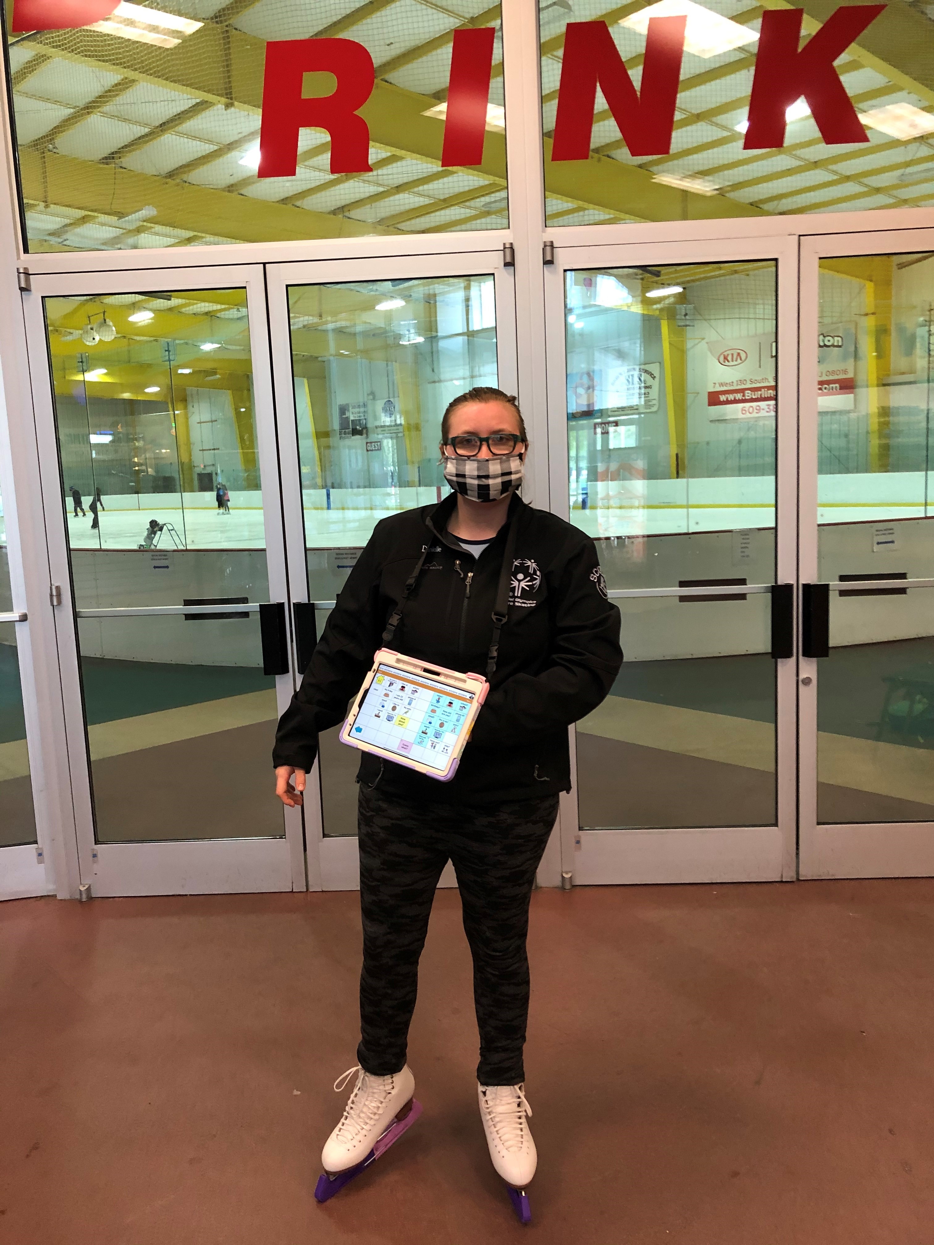 young woman with ipad and figure skates standing in front of ice skating rink