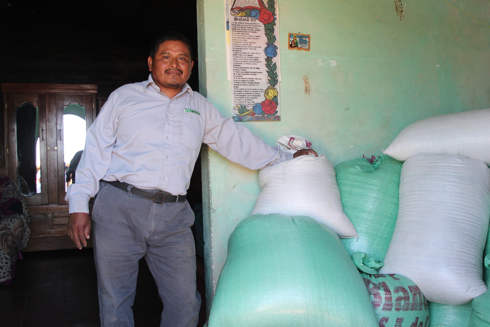 Jose stands next to bags of beans stored in the living room of his home. It’s the only place he has to store the beans to keep them safe from insects.