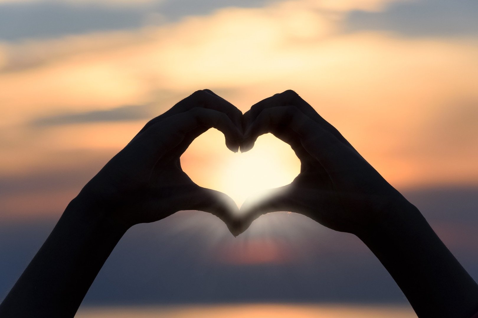 sunset viewed through 2 hands forming a heart