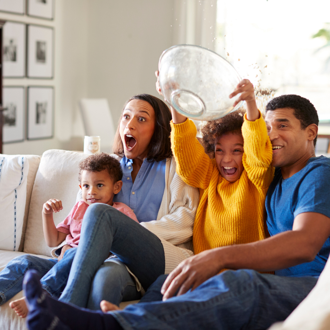 family watching TV together, one child spilling popcorn