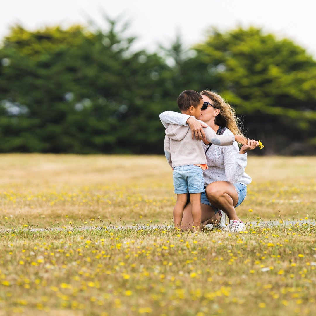 mom kissing little boy after he gives her a handful of dandelions