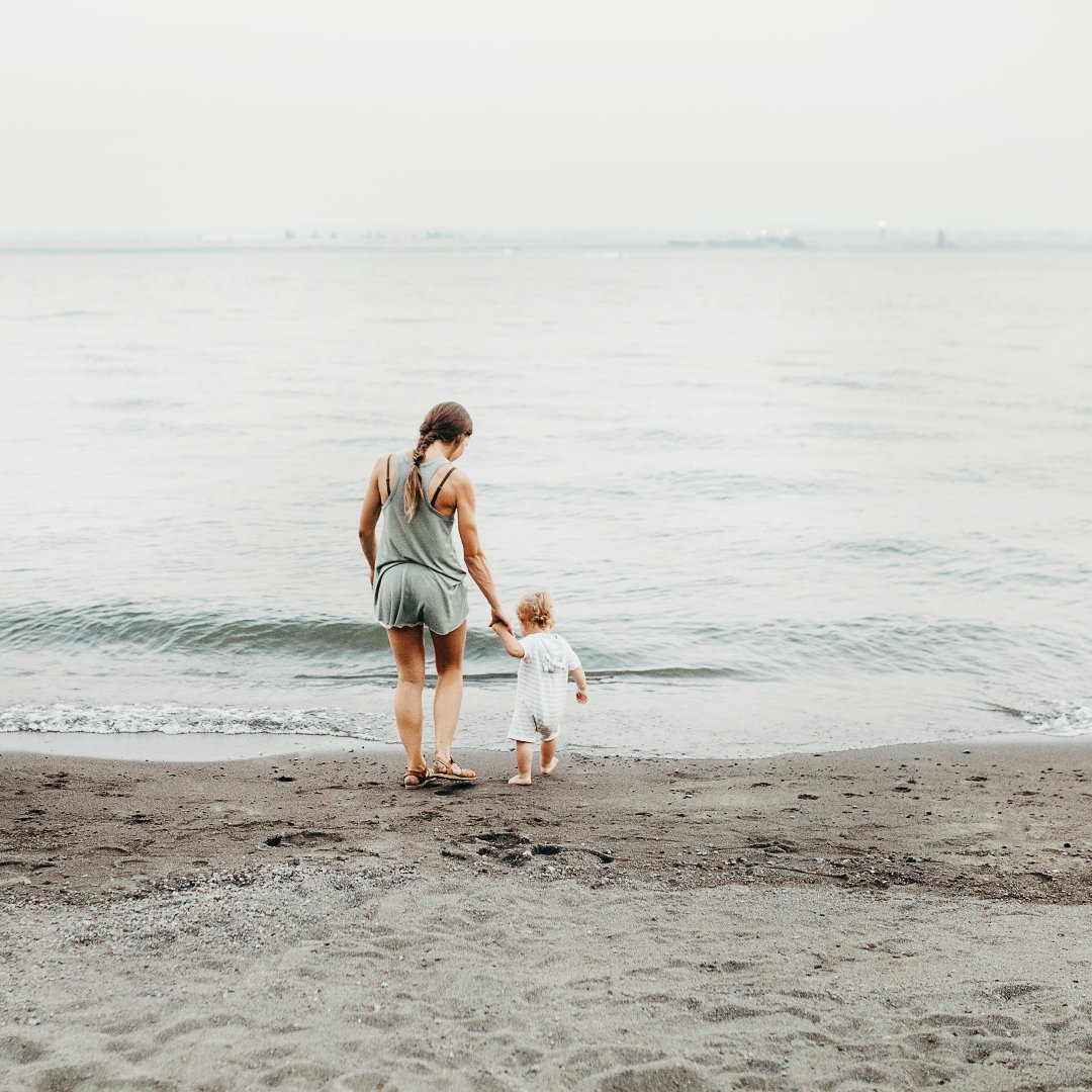 Mom holding toddler's hand on shore of a lake