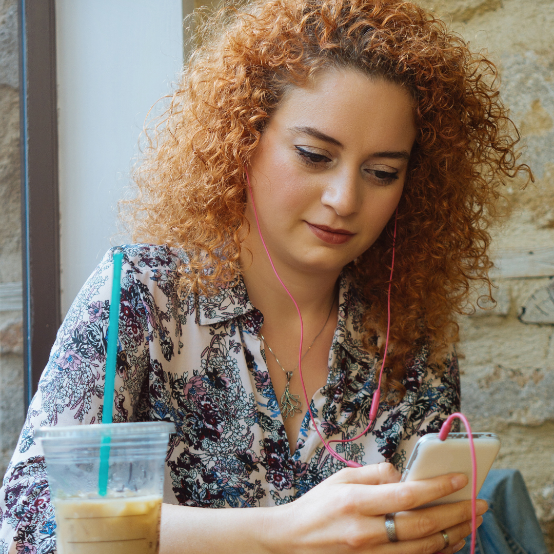 woman using earbuds to listen to podcast in coffee shop