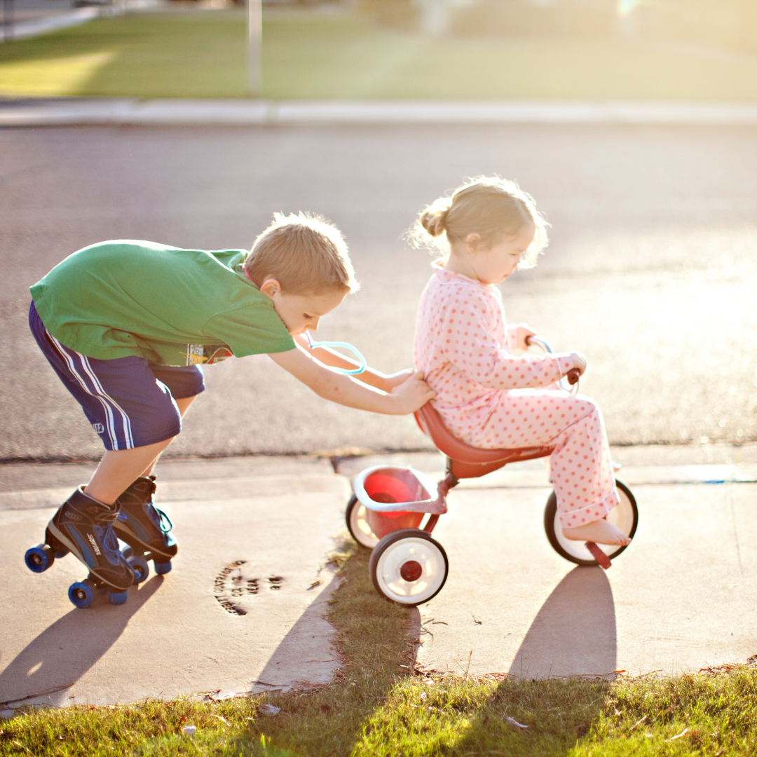 big brother on roller skates pushing little sister on tricycle