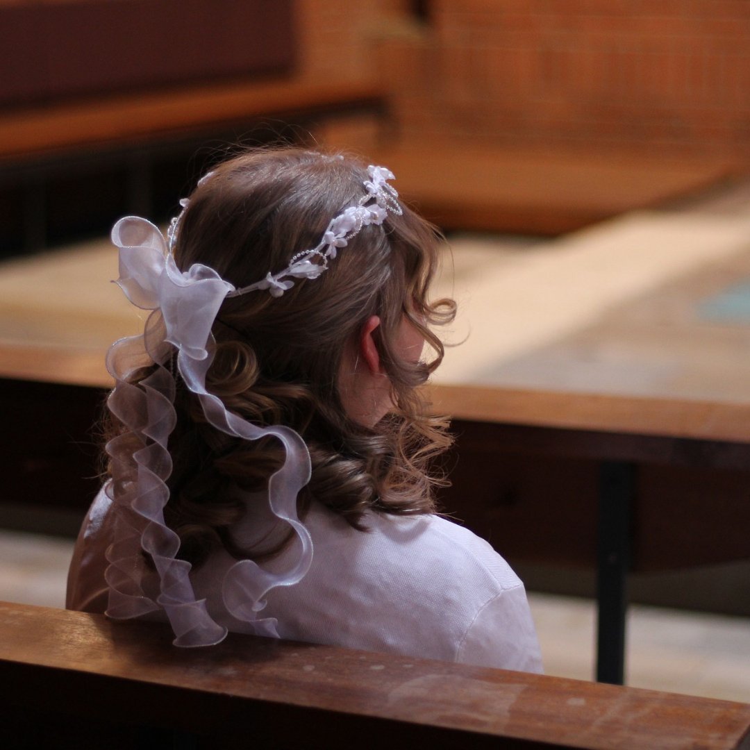 girl dressed for First Communion, sitting alone in a church