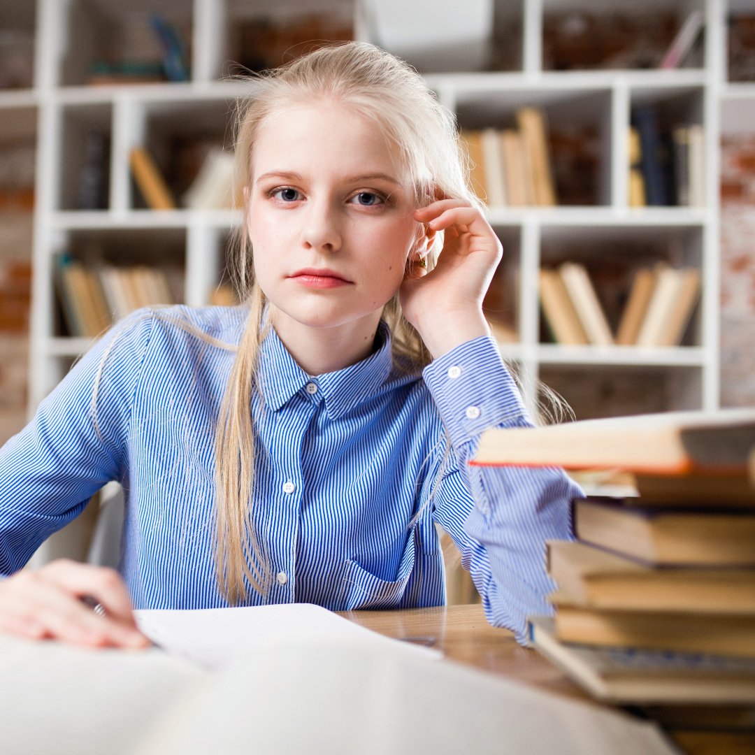 girl sitting at table surrounded by schoolbooks