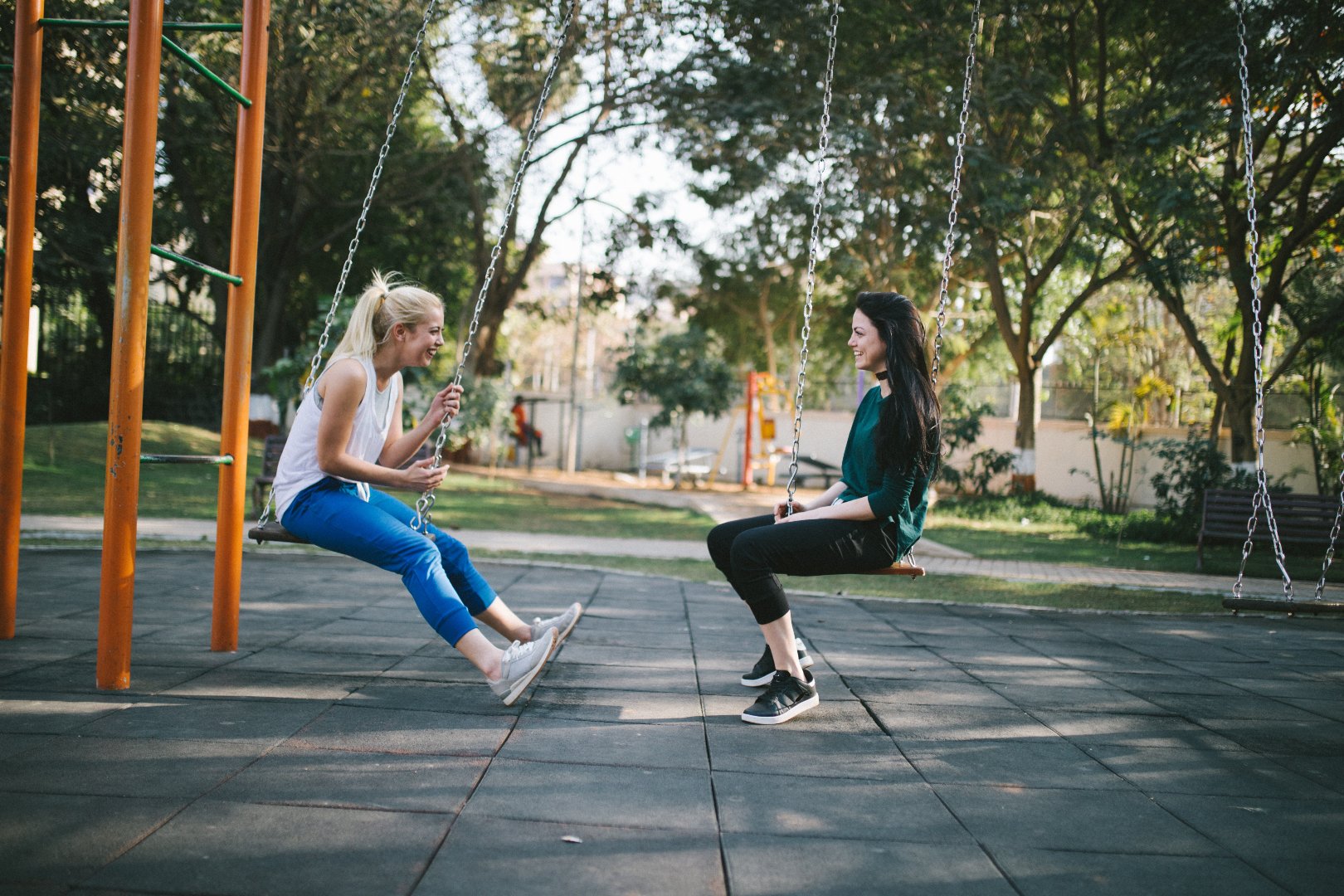 2 women sitting on playground swings and talking