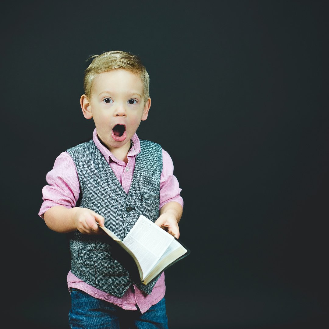 little boy holding book, looking surprised