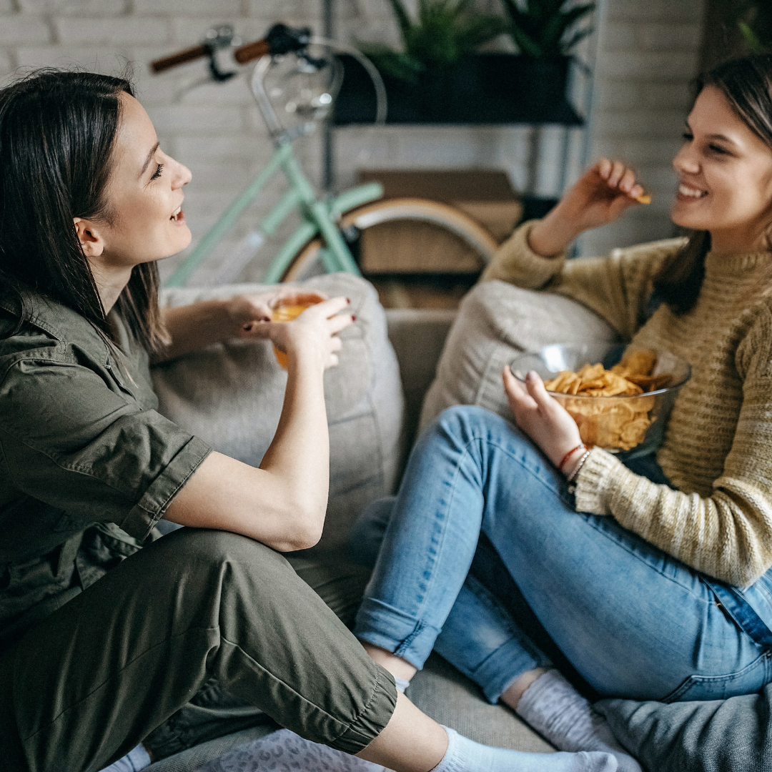 2 women sitting, talking, with drinks and snacks