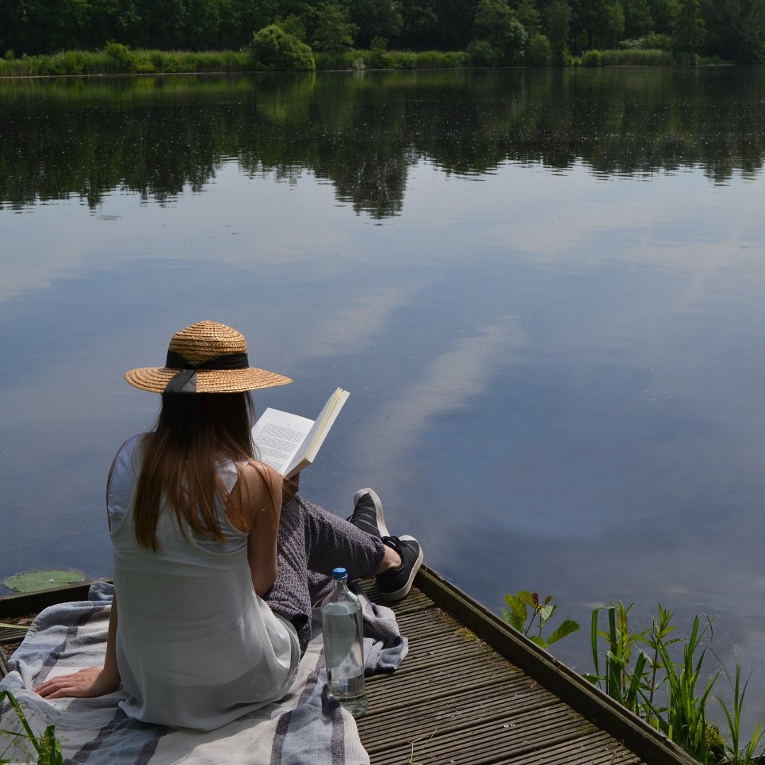 woman reading at a dock beside a lake