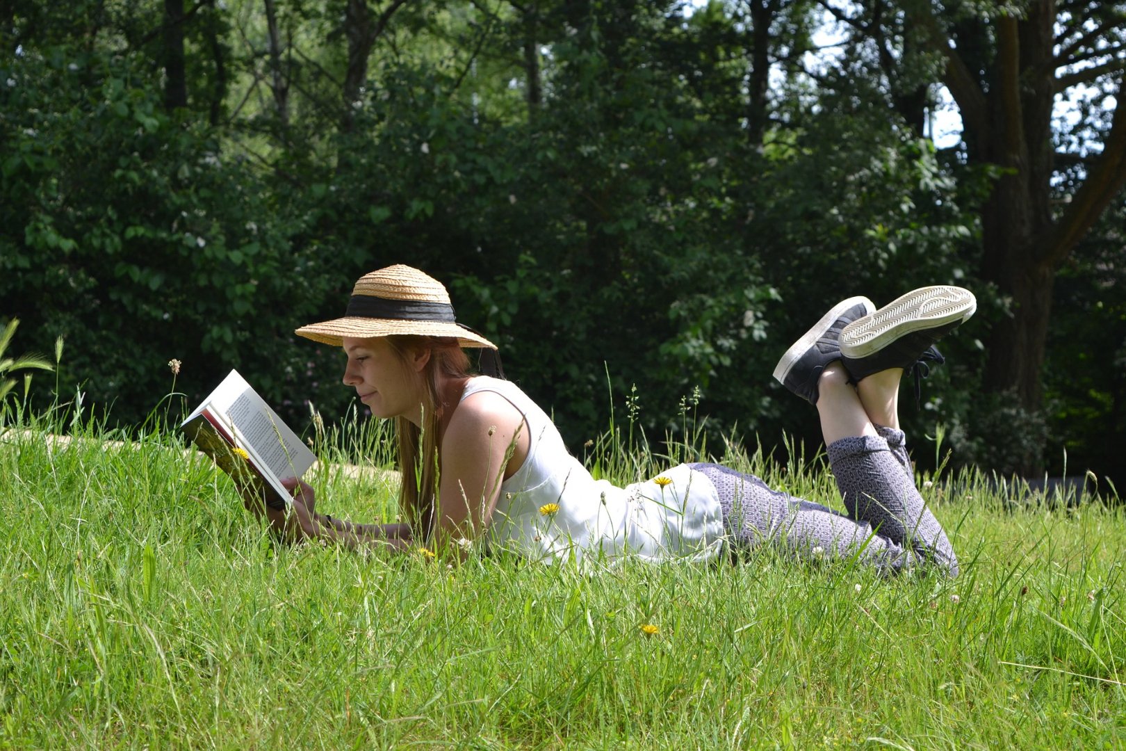 woman wearing a sun hat, reading in the grass