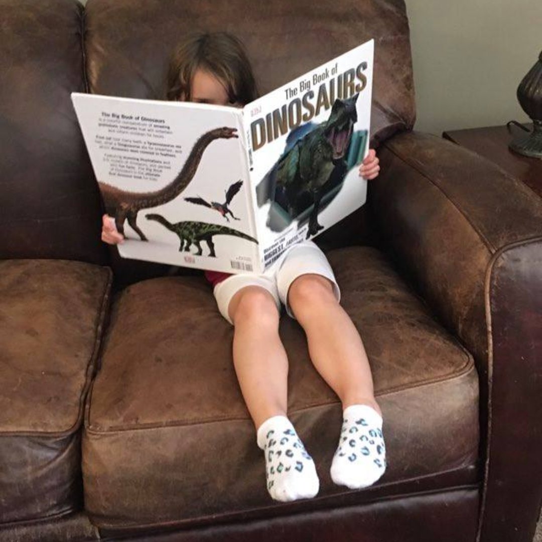 little girl reading book about dinosaurs