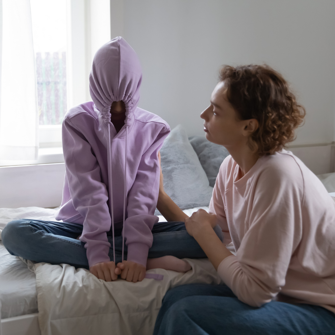 mom talking to teenager who's hiding inside a hoodie