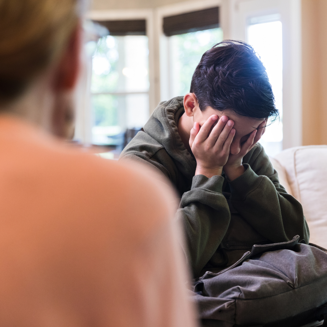 mom seen from back, talking to teen boy who's covering his face