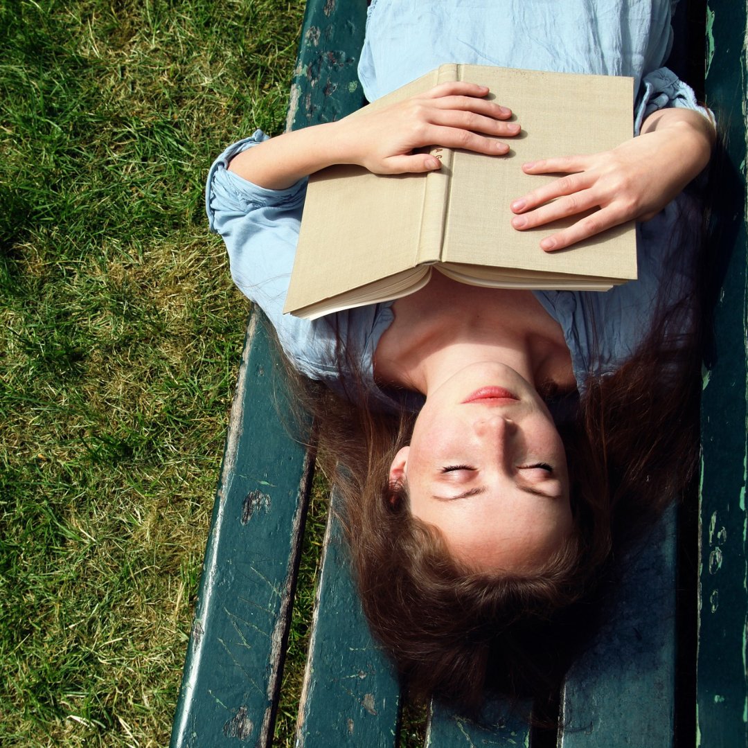 woman asleep on a bench, holding a book