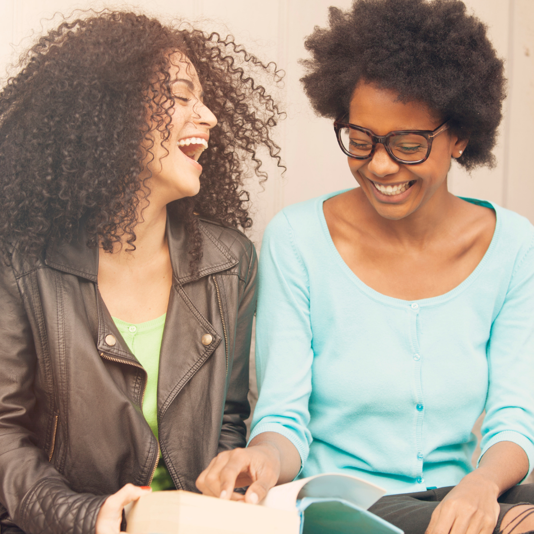2 women reading a book together and laughing