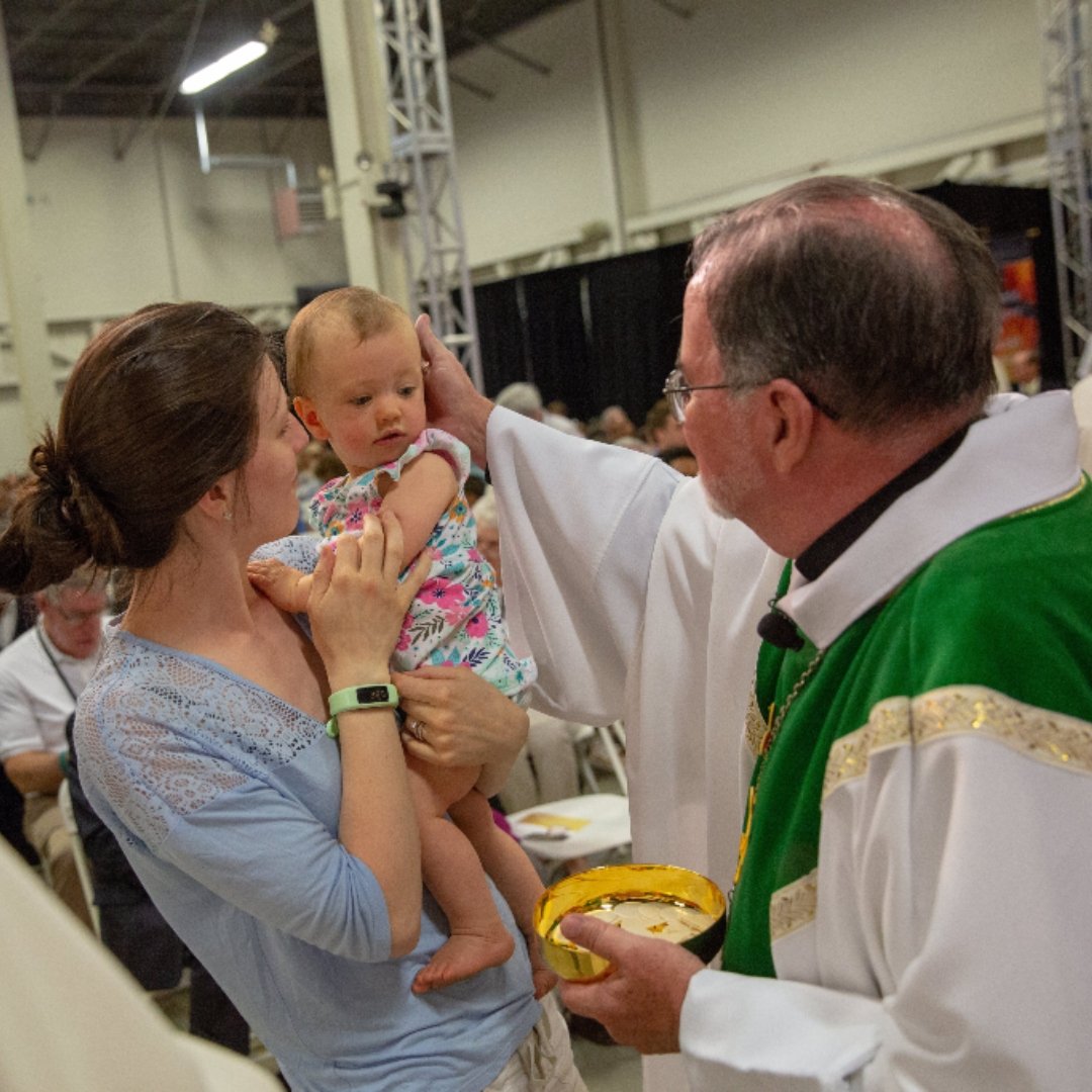 priest blessing baby held by Mom