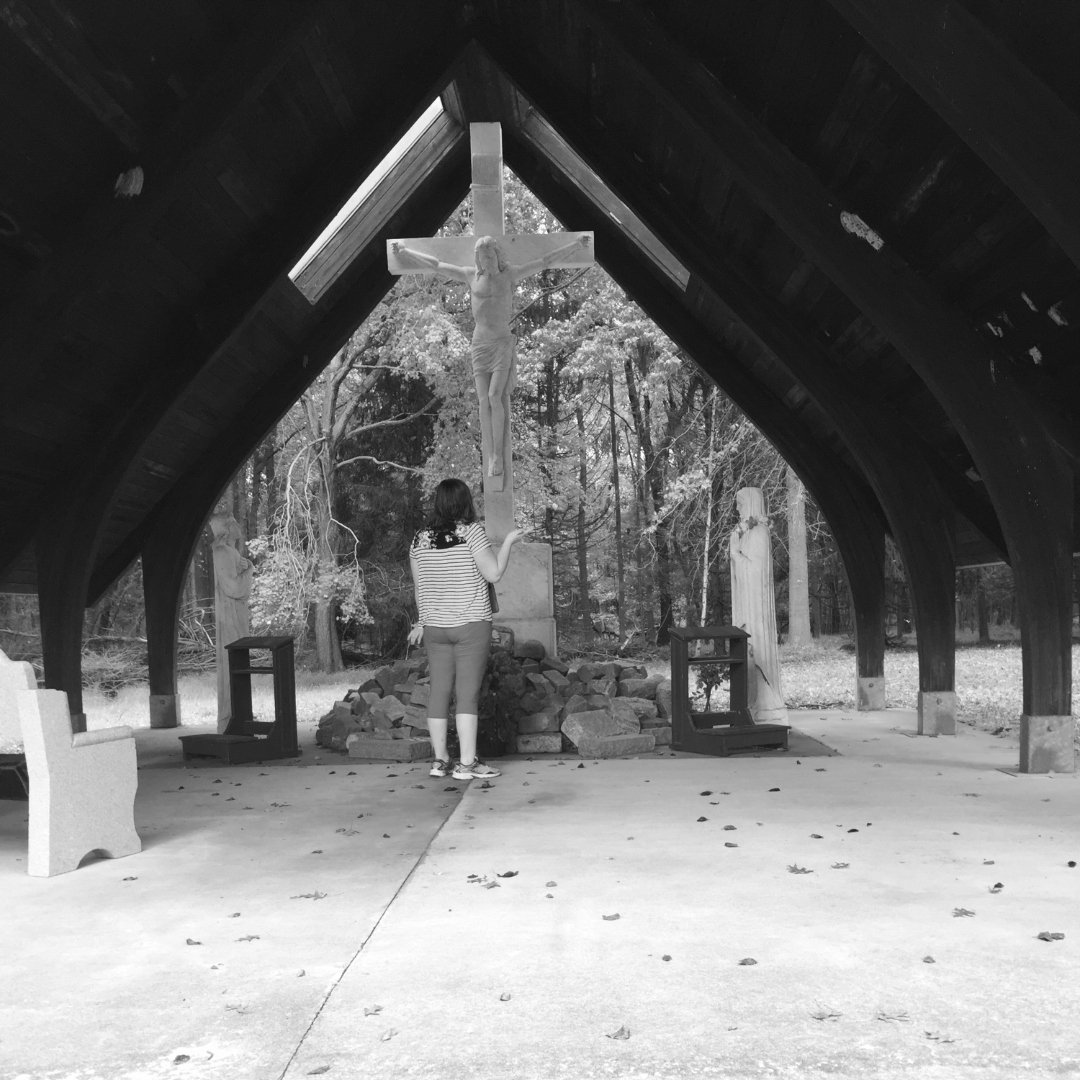 girl praying in front of cross and statue