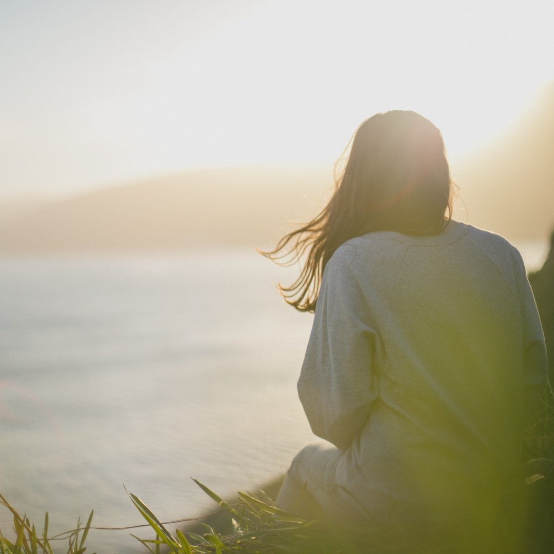 woman sitting near a shoreline at sunset