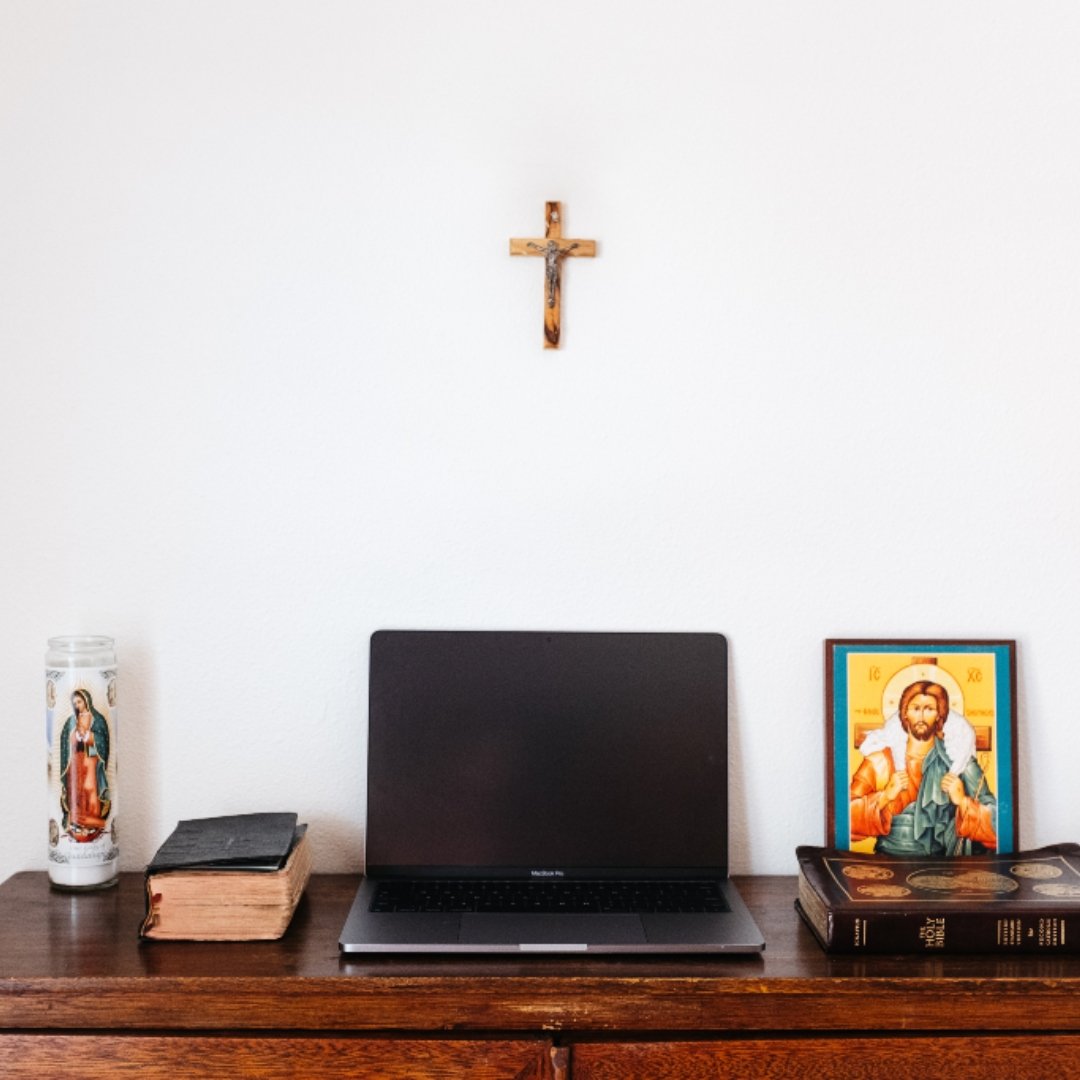 Catholic icon, candle, Bible, and crucifix surrounding a computer