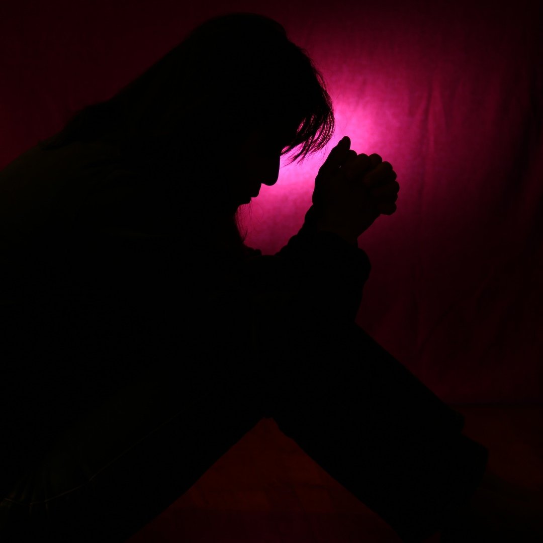 silhouette of woman praying, backlit in front of a pink curtain