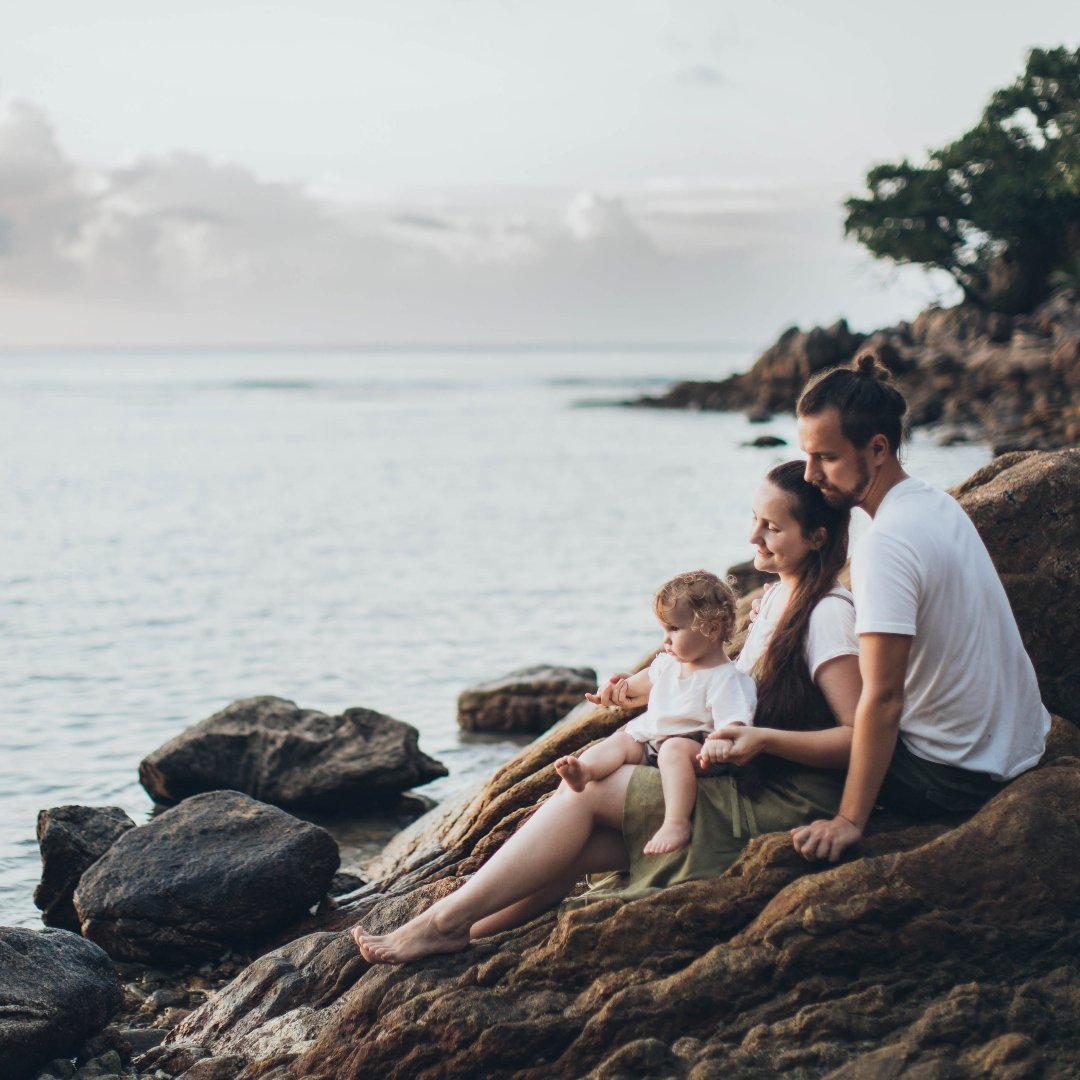 family sitting on side of a lake