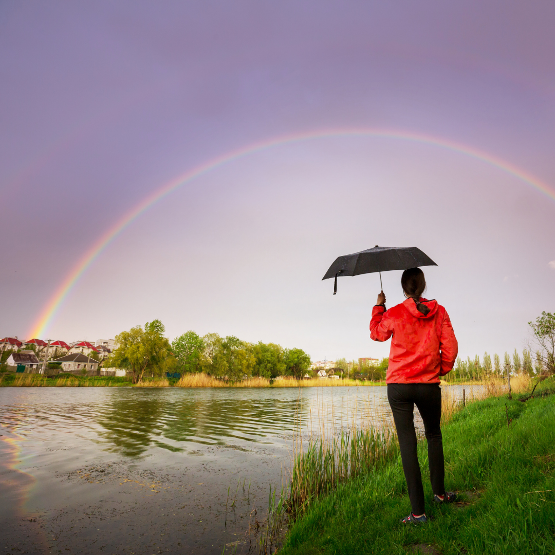 woman with umbrella looking at a double rainbow