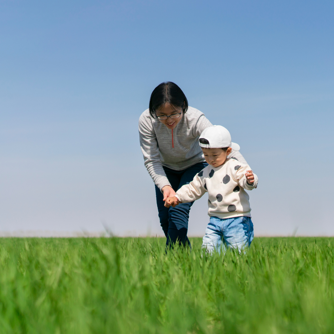 mom helping toddler walk across a field