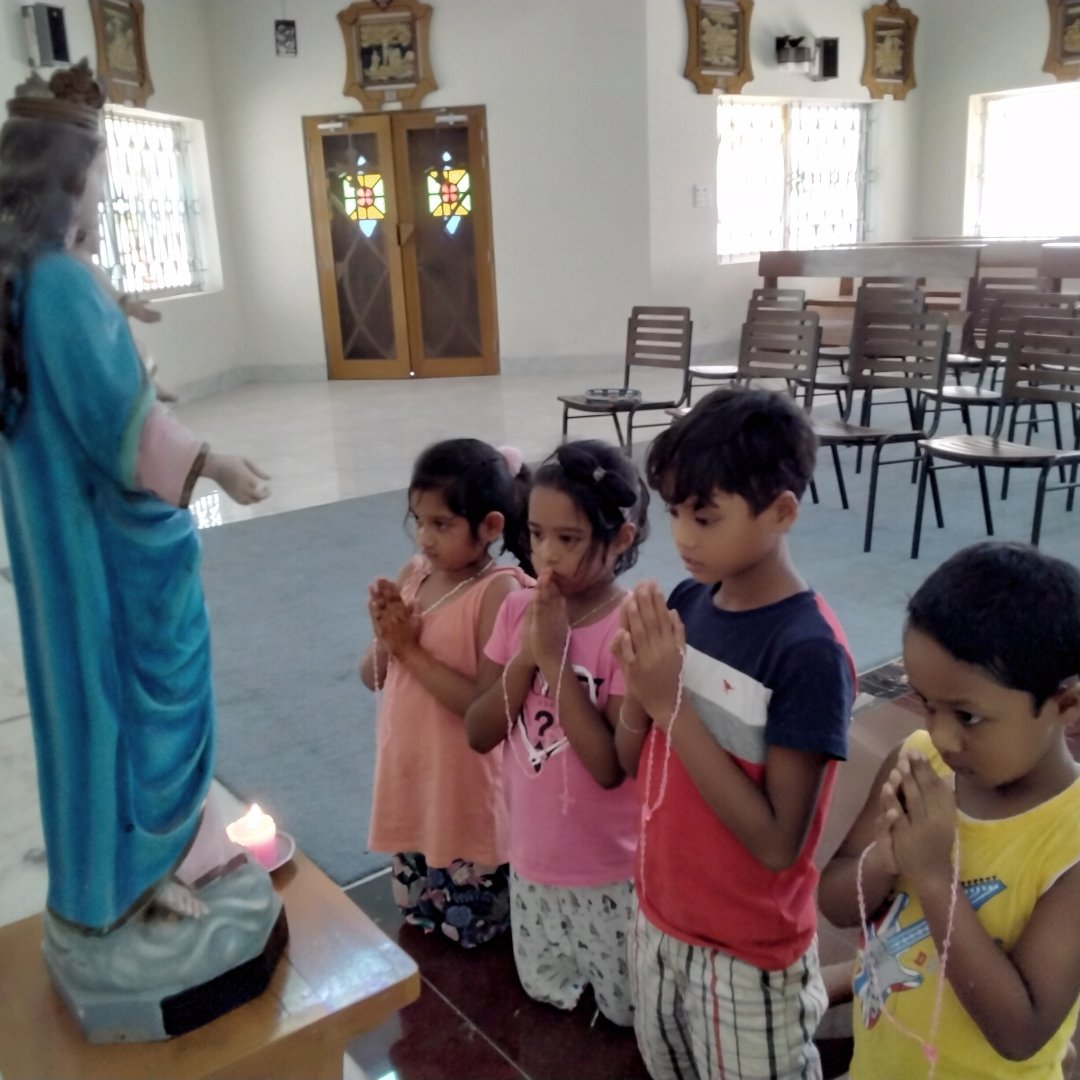 children praying in front of a statue of Mary