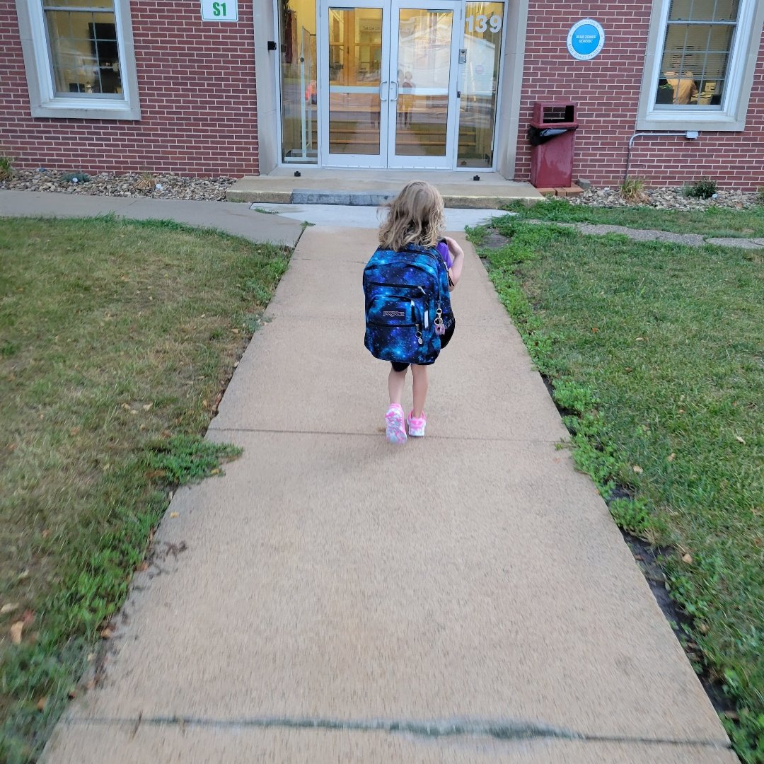 little girl wearing a backpack walking into school