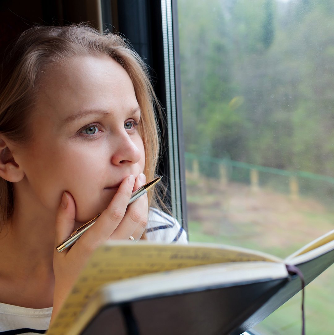 woman looking out the window and writing in a journal