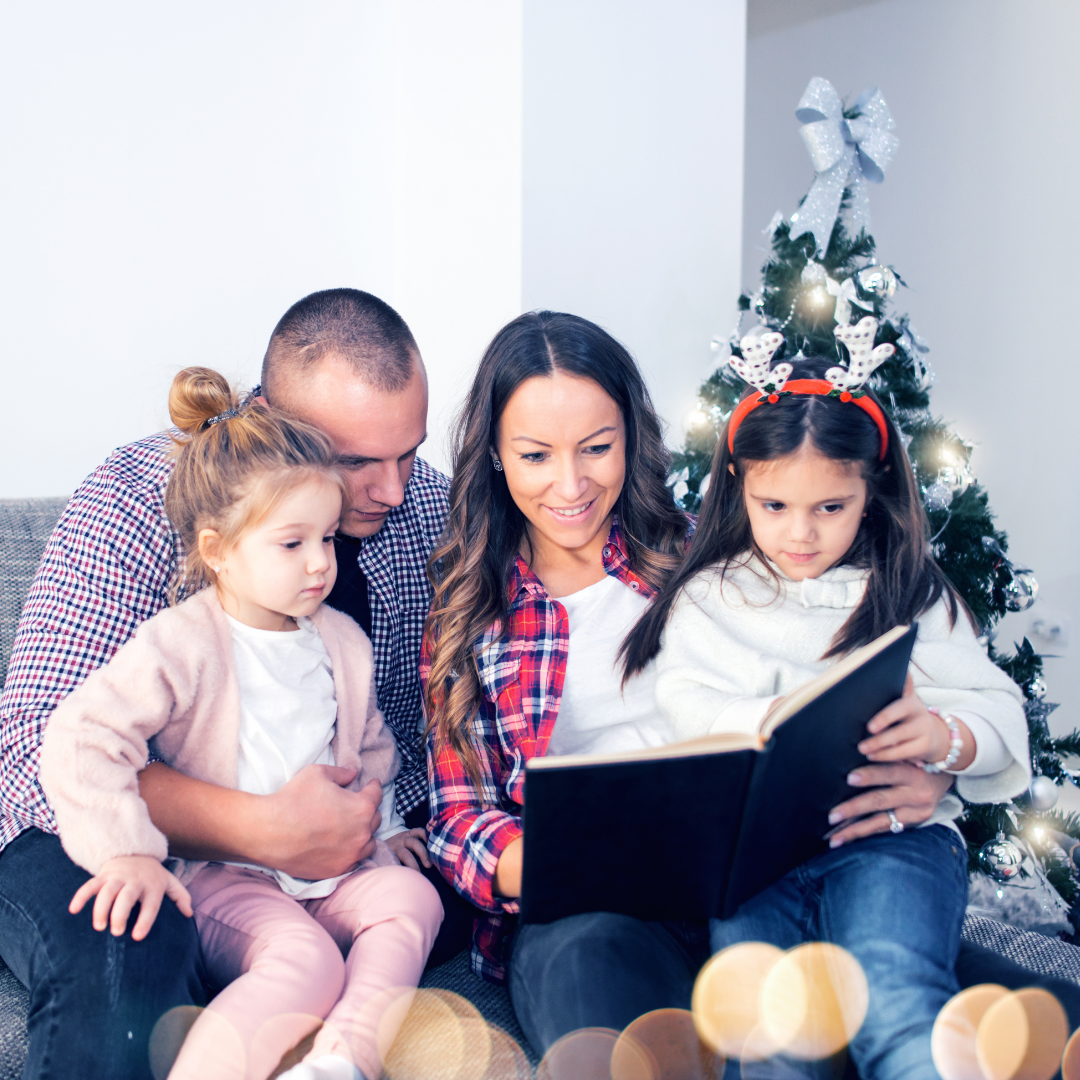 family reading book in front of Christmas tree